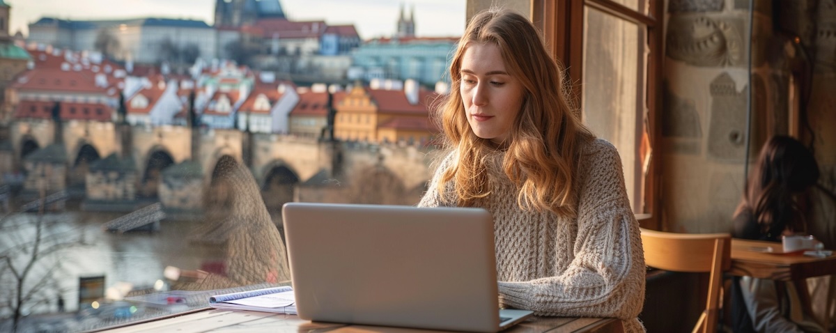 Norsk kvinne som lærer tsjekkisk på laptop med Karlsbroen i Praha i bakgrunnen